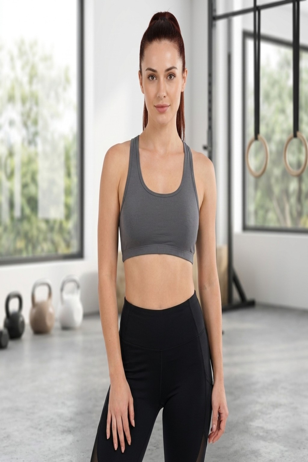 Woman in a gray sports bra and black leggings standing in a gym.